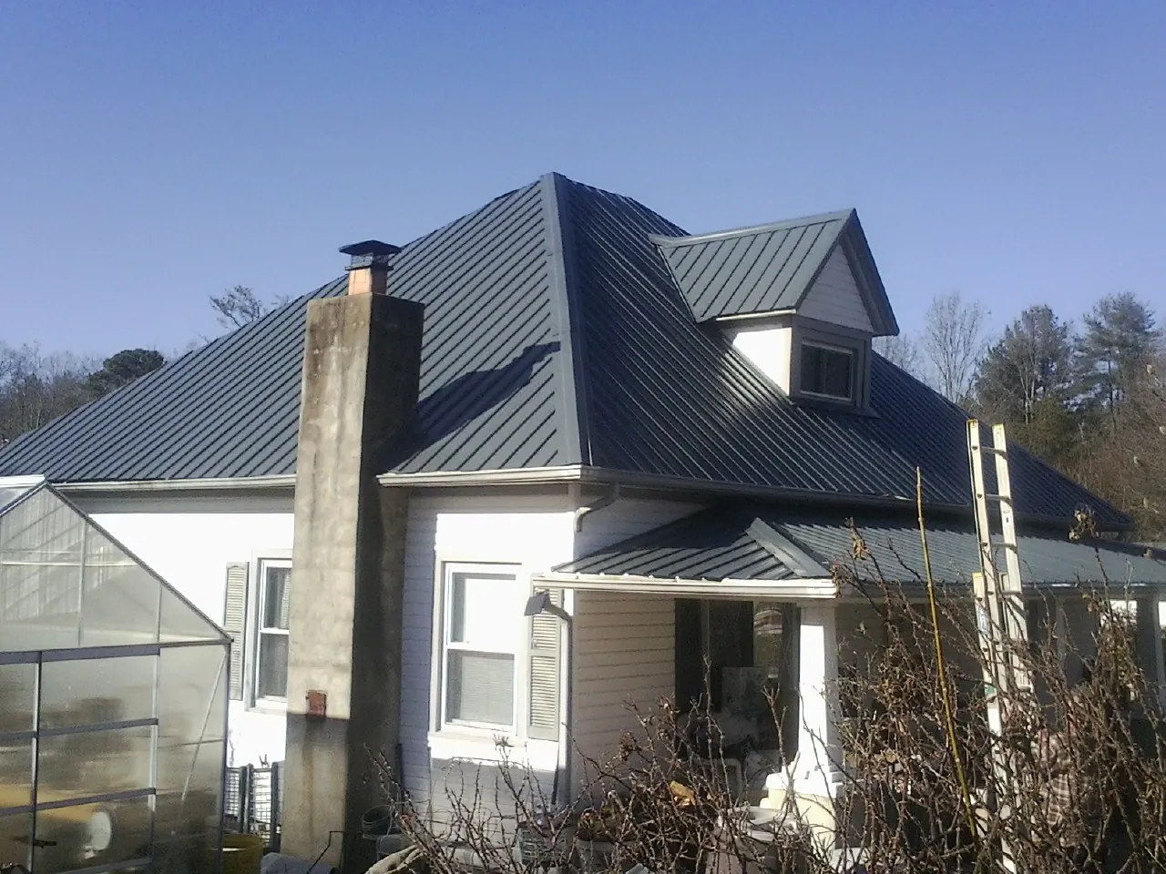 Dark blue standing seam metal roof on a white farmhouse with dormer — Slate & Tile Roof Repair by Roofing Brothers in Cost