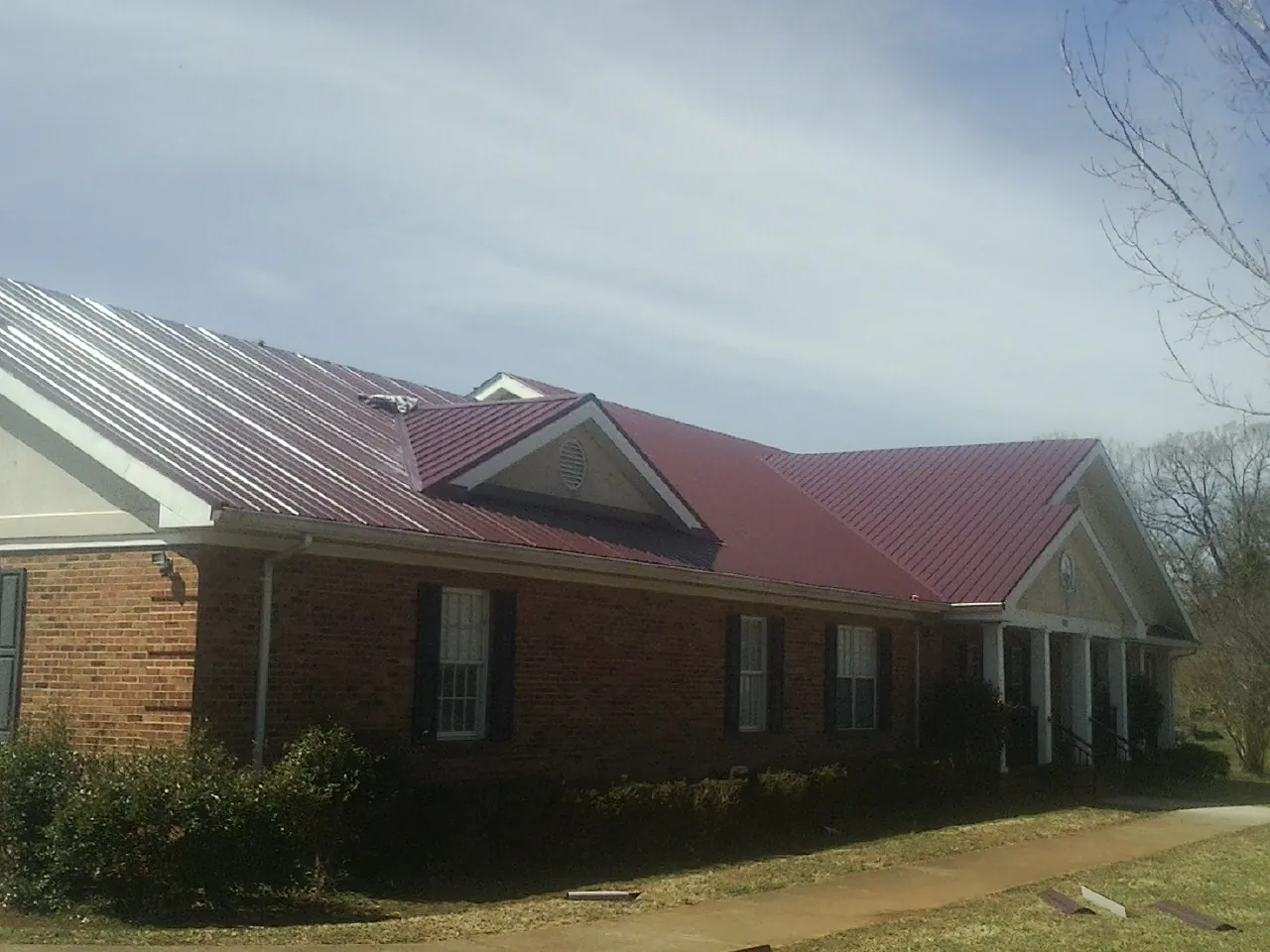 Red metal roof with gabled entries on a long brick building, from a Hail Damage Roof Repair job in Cost