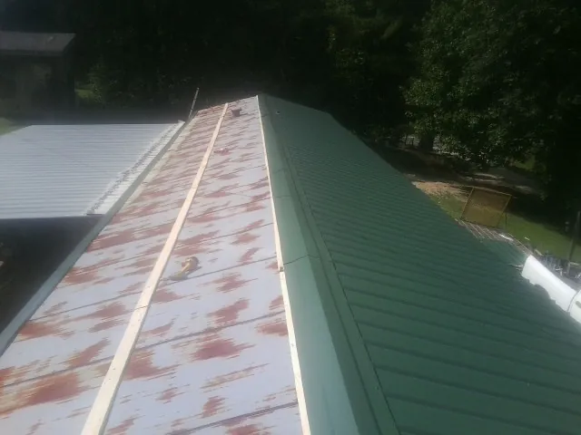Old rusted panels beside newly installed green metal roofing — Wind Damage Roof Repair by Roofing Brothers in Cost