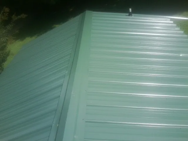 New green metal panels meeting at the ridge of a roof — Flat Roof Repair work by our crew in Cost