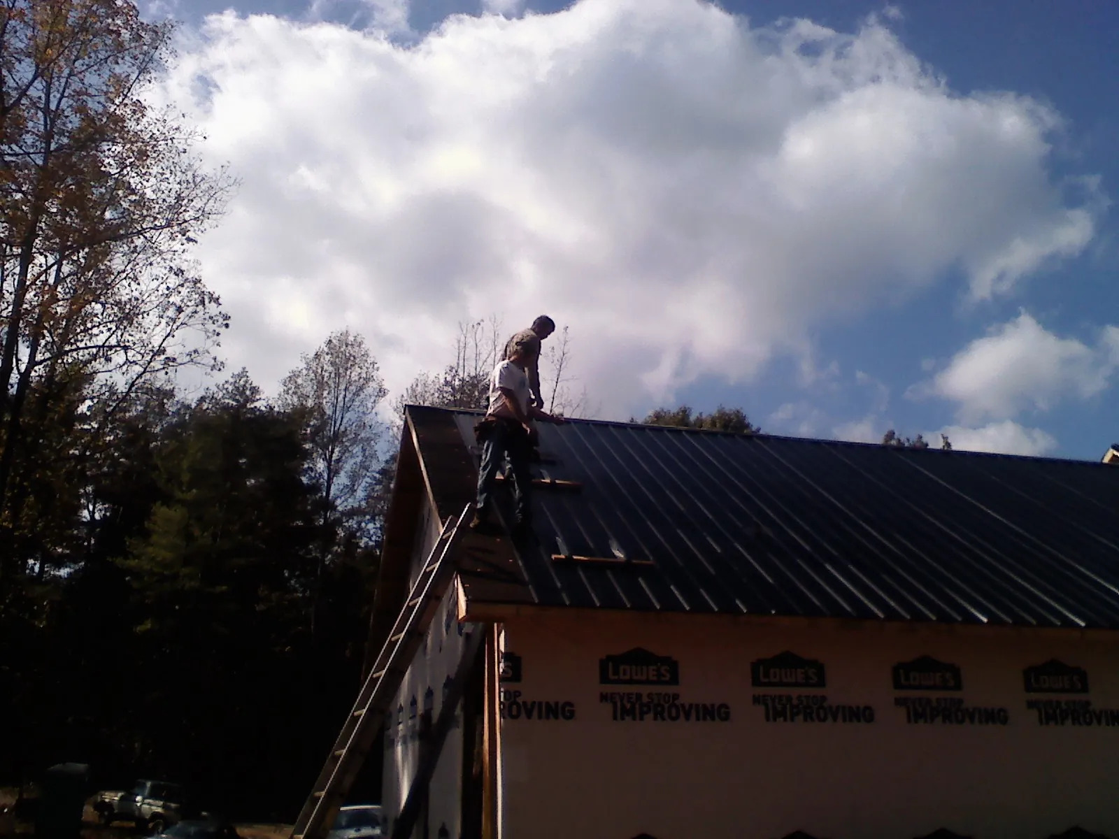 Roofer fastening dark metal panels high against a cloudy sky, from a Roof Inspection job in Cost