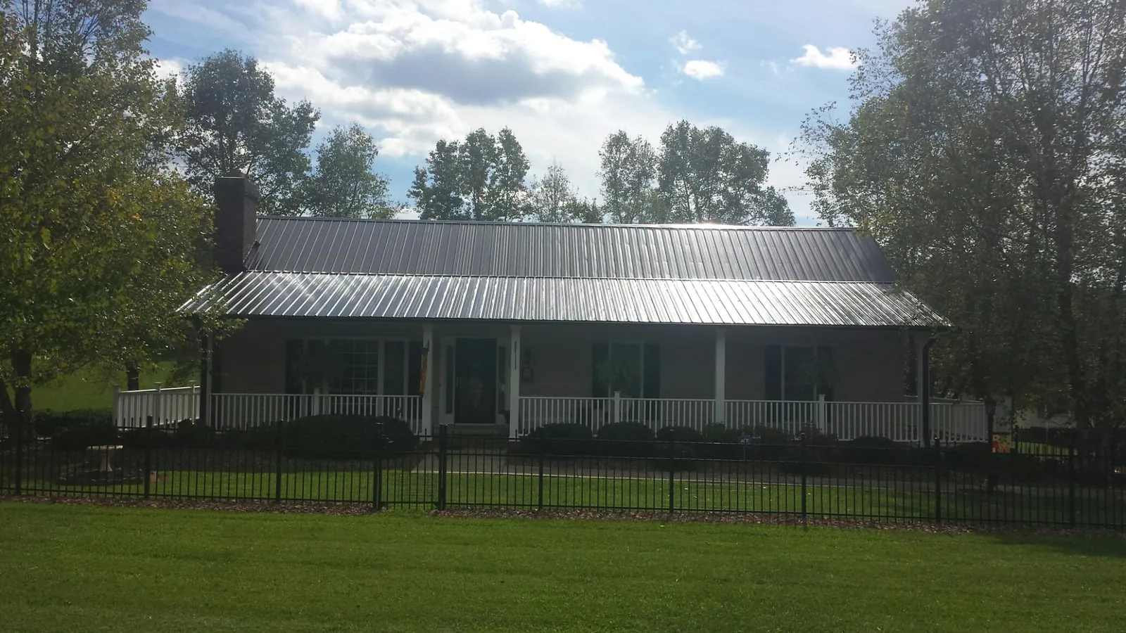 Gray metal roof on a brick ranch with a full width front porch — Gutter Guard Installation work by our crew in Cost