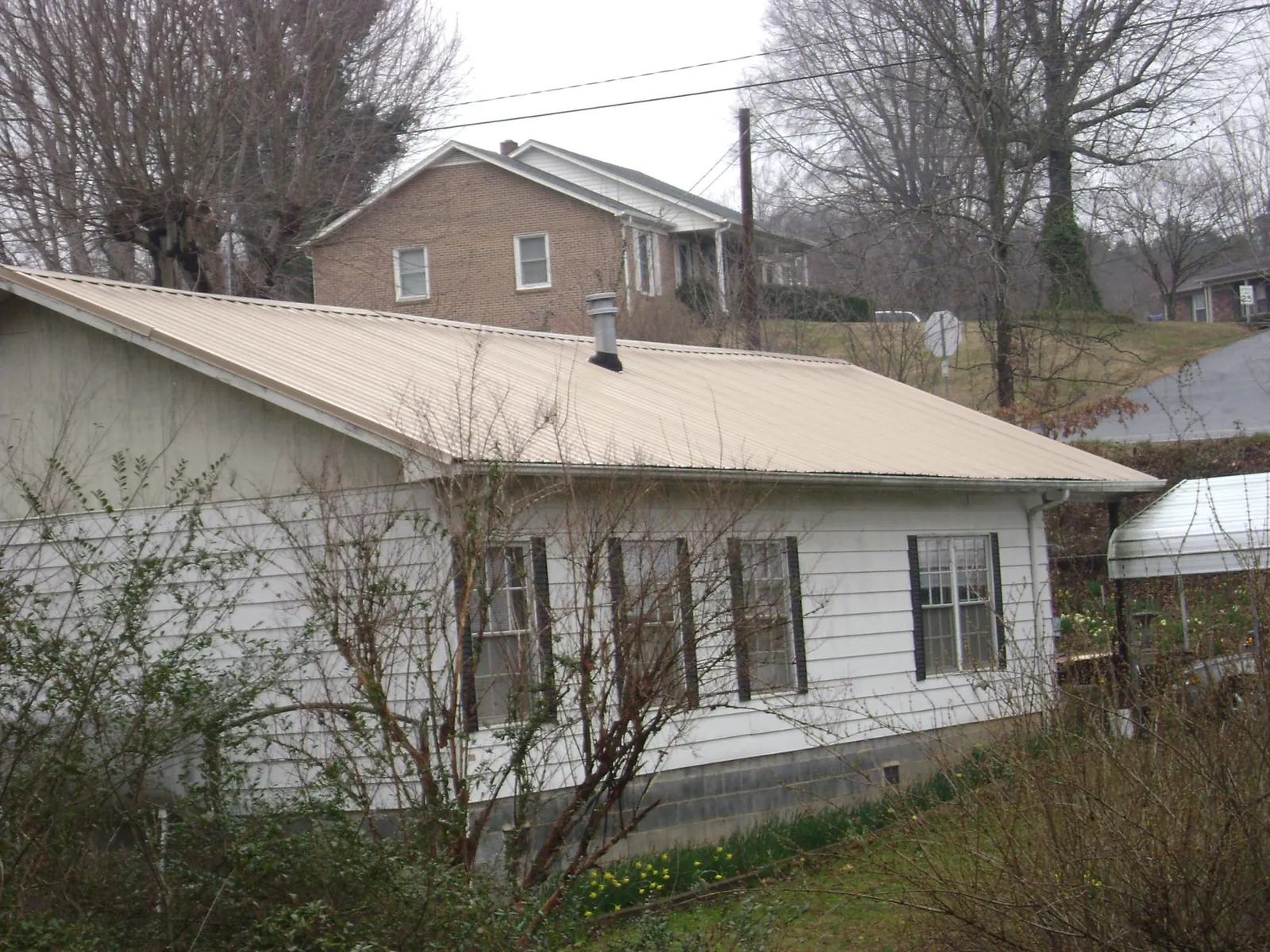 Tan metal roof on a white sided house set into a hillside — Commercial Roofing by Roofing Brothers in Cost