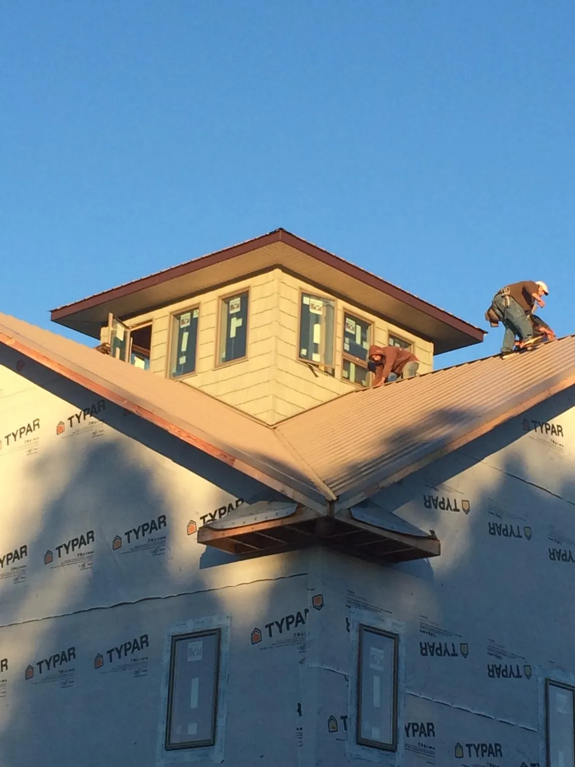 Roofers working around a rooftop cupola on a new metal roof at sunset — Roof Waterproofing in Cost by Roofing Brothers